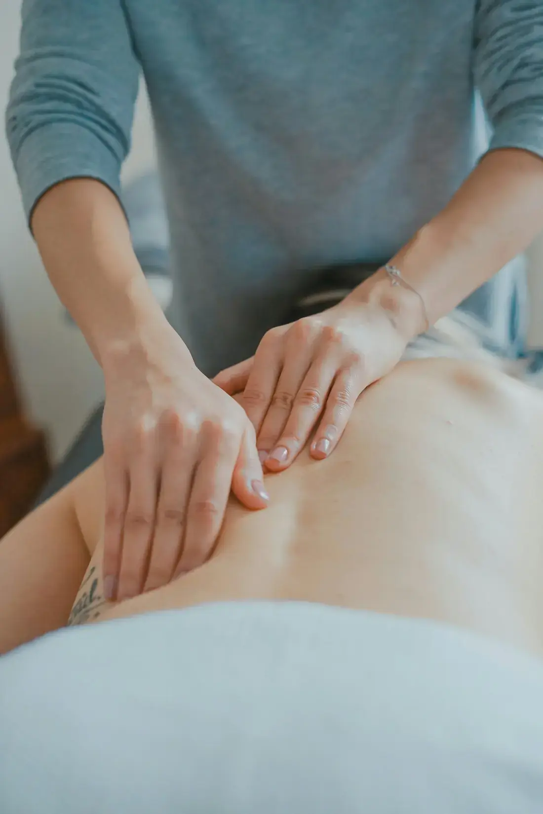 Two hands rest gently on a woman's back during a calm bodywork session.