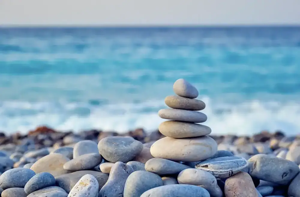 A stack of smooth balanced pebbles on a pebble beach, with the sea softly out of focus behind.