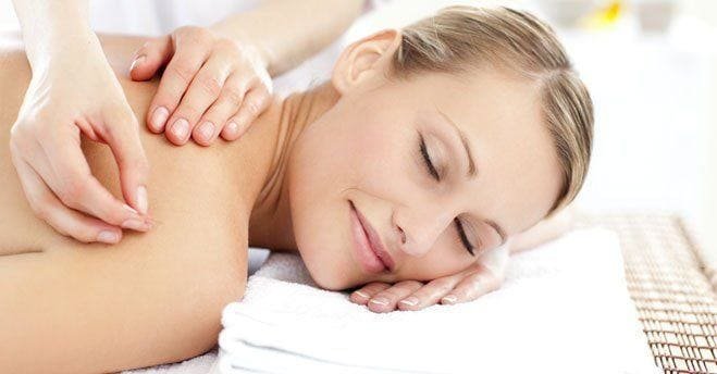A woman resting on a treatment couch with her eyes closed while an acupuncture needle is placed in her upper back.
