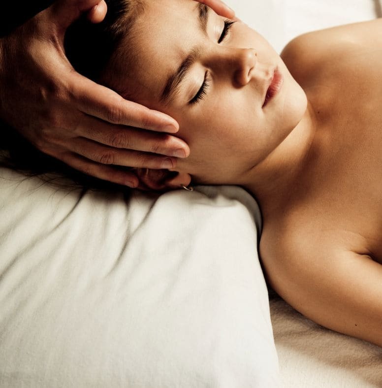 A child resting on a white pillow with eyes closed while hands gently cradle the head.