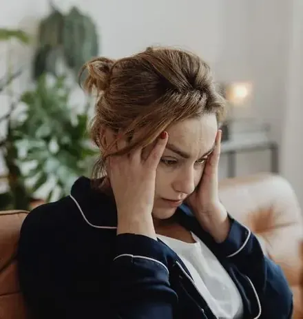 A woman sits with her head in her hands, eyes closed, a look of tension and overwhelm on her face.