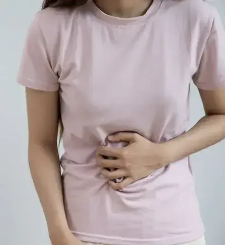 A woman in a pink t-shirt gently holds her stomach with both hands.