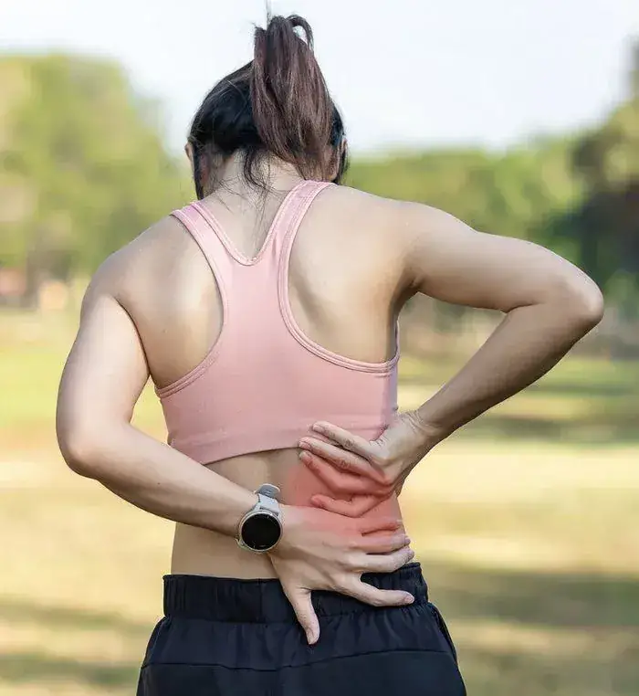 A woman seen from behind presses one hand into her lower back, showing a highlighted area of pain.