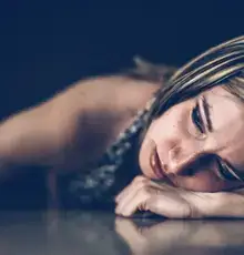 A woman lies face down, head resting on her arm, in quiet distress.