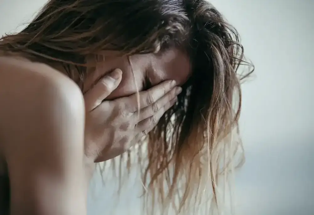 A woman covers her face with her hand, head bowed, in visible distress.