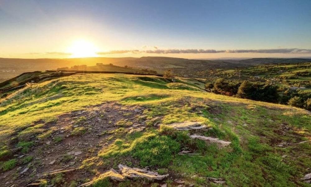 The grassy summit of Eccles Pike at sunset, with golden light over the hills and wooded valleys of the High Peak.