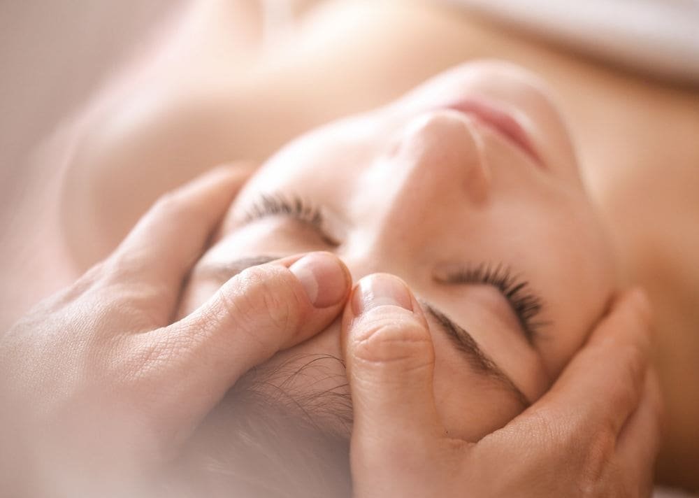 A therapist's hands gently holding a woman's face during a relaxing facial massage.