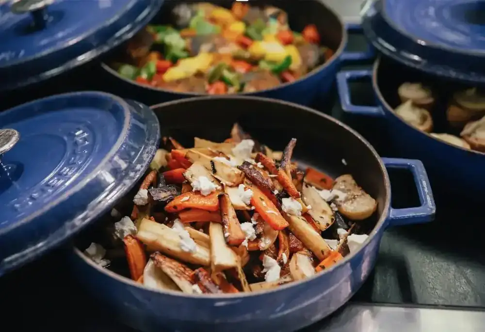 Roasted root vegetables with feta in a blue cast-iron pot, part of a shared spread.