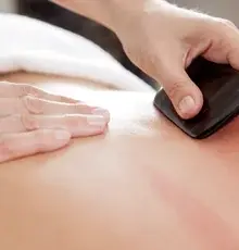 A gua sha tool being drawn across someone's upper back during treatment.