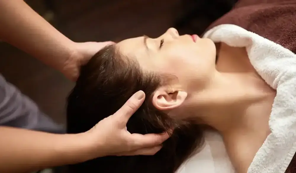 A practitioner’s hands cradling a woman’s head during a gentle head and scalp massage.