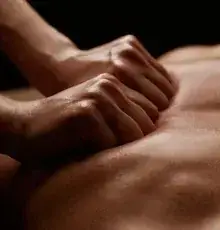 Hands massage a person's upper back during a bodywork treatment.