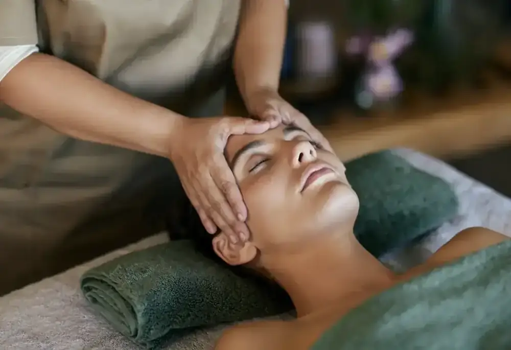 A practitioner's hands resting on a relaxed woman's forehead during a head massage.
