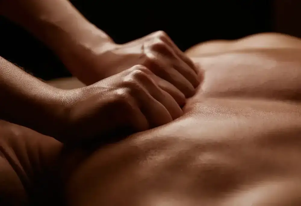 Hands press firmly into a person's upper back during a bodywork treatment.