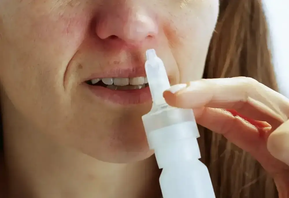 A close-up of a woman using a nasal spray.