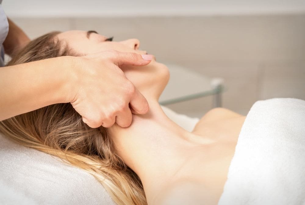 A therapist's hand gently working on the neck and jaw of a woman lying on a treatment couch.
