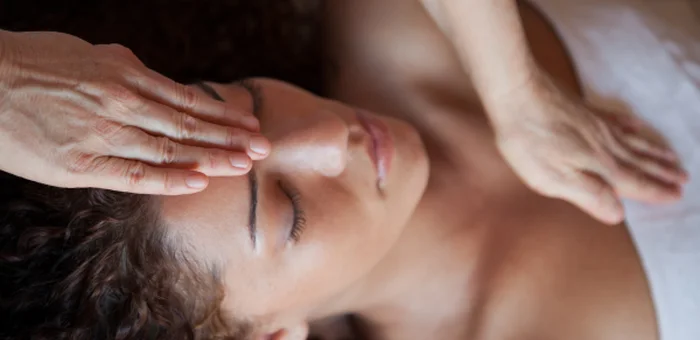 A practitioner's hands rest gently on a relaxed woman's forehead and chest during treatment.