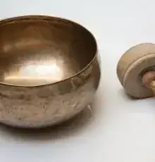 A brass singing bowl and wooden mallet used in sound therapy.