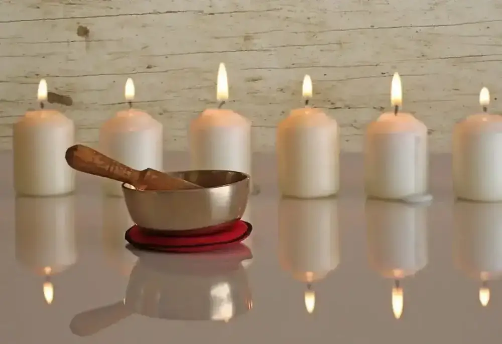 A brass singing bowl and wooden mallet resting beside a row of lit candles.