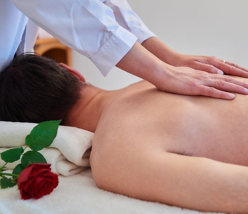 Ela’s hands resting gently on a client’s back during treatment, a red rose on the couch.