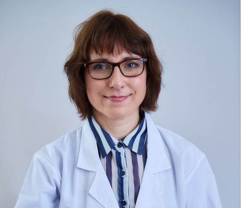 Ela in a white coat, smiling warmly at the camera.