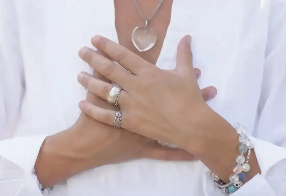 A close-up of a hand resting in a meditation mudra, seated cross-legged in soft light.