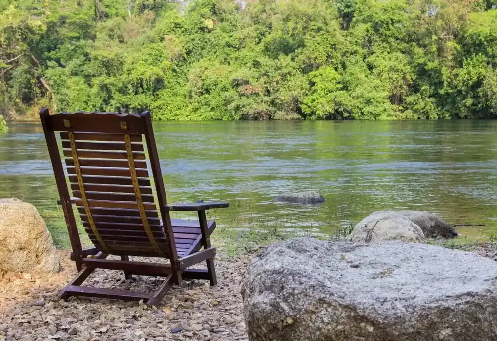 A wooden deckchair beside a quiet river.