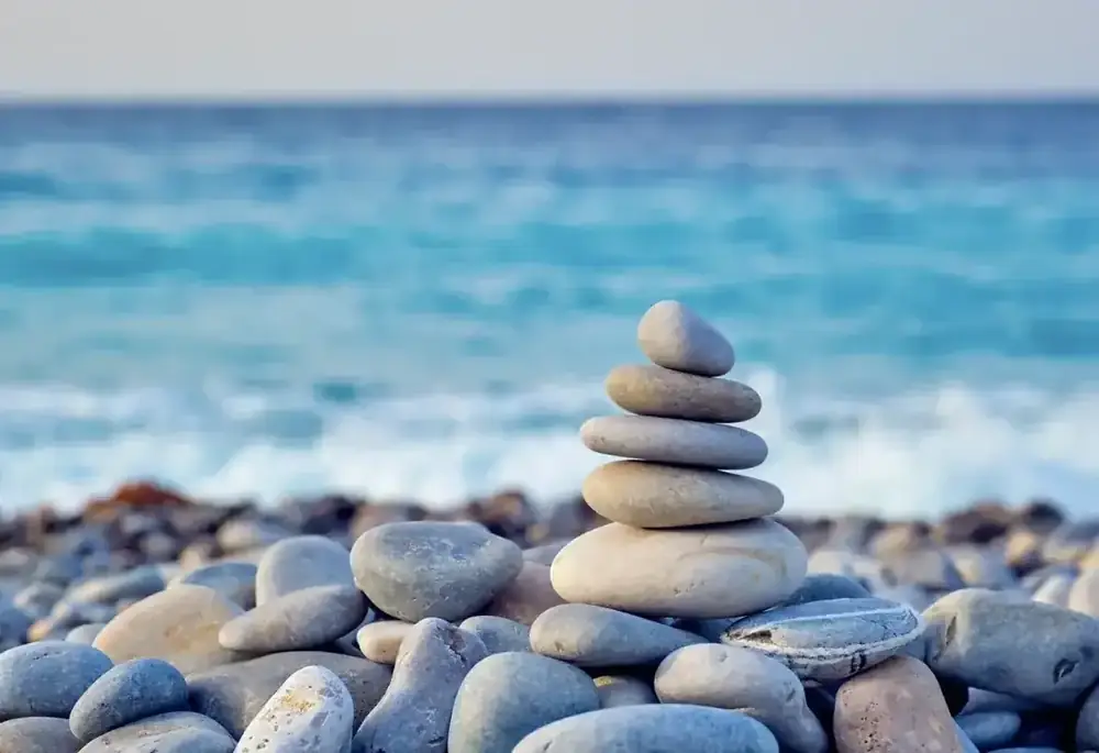 A stack of smooth pebbles balanced on a beach, waves in the background.